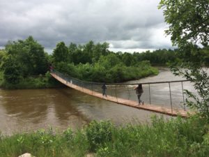 Walkers cross a rope bridge over the Roseau River in Manitoba