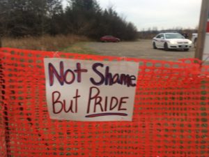 picture shows a banner reading 'not shame but pride' hanging on an orange snow fence outside the park, with a police vehicle visible on the other side of the fence