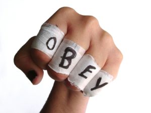 A white-skinned hand, making a fist, with the word OBEY written on tape wrapped around each finger